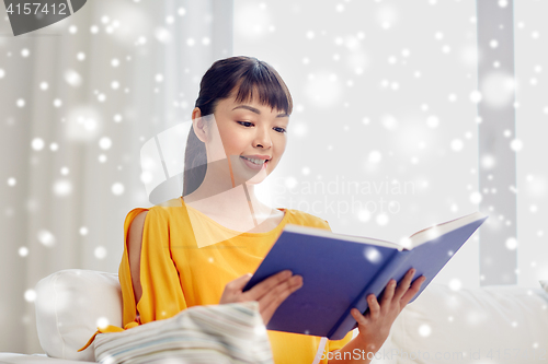 Image of smiling young asian woman reading book at home