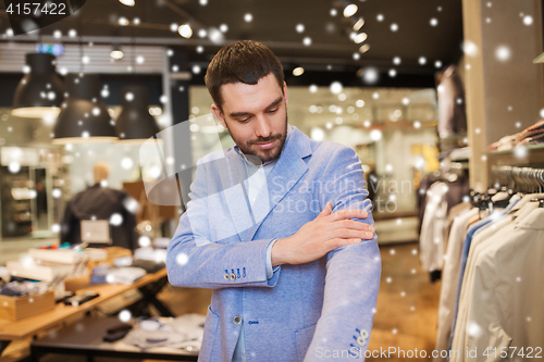 Image of happy young man trying jacket on in clothing store