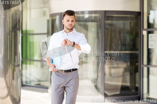 Image of man with folder looking at wristwatch on street