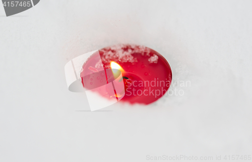 Image of burning christmas candle on snow in winter