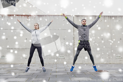 Image of happy man and woman jumping outdoors