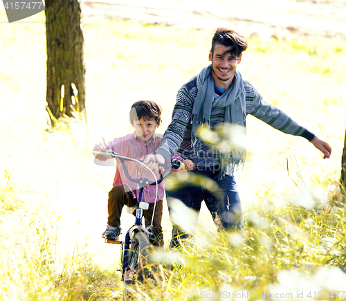 Image of father learning his son to ride on bicycle outside, real happy f