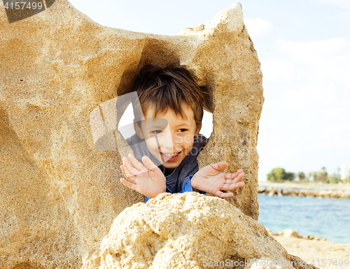 Image of little cute boy on sea coast thumbs up playing with rocks