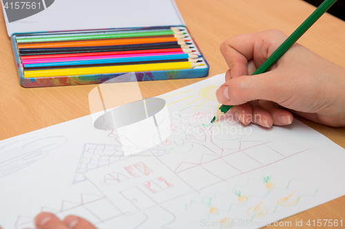 Image of The girl draws a picture with colored pencils on paper, close-up