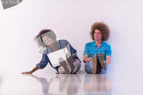 Image of multiethnic couple sitting on the floor with a laptop and tablet