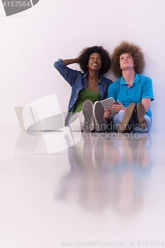 Image of multiethnic couple sitting on the floor with a laptop and tablet