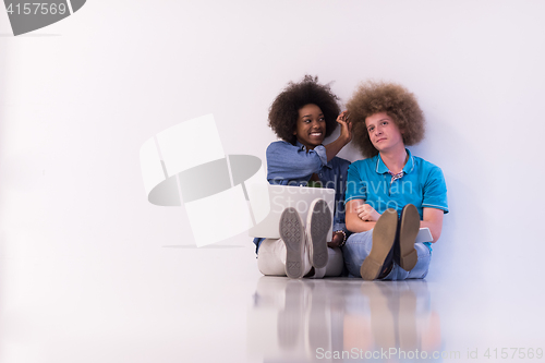 Image of multiethnic couple sitting on the floor with a laptop and tablet