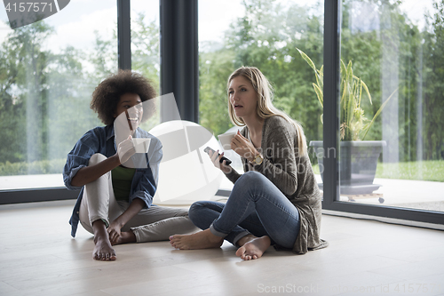 Image of multiethnic women sit on the floor and drinking coffee