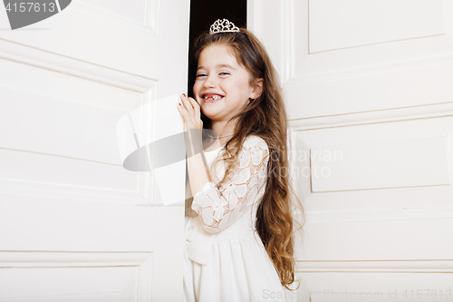 Image of little cute girl at home, opening door well-dressed in white dress, adorable milk fairy teeth