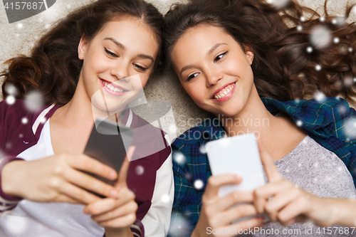 Image of happy teenage girls lying on floor with smartphone