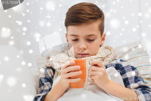 Image of ill boy with flu in scarf drinking tea at home