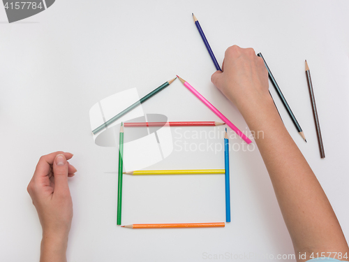 Image of Women\'s hands are building a wooden house from pencils