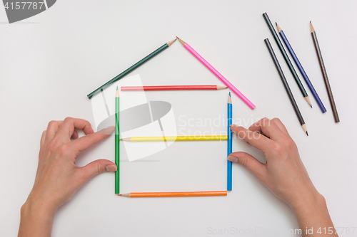 Image of closeup Hands build a house on a piece of paper from the crayons, erecting walls