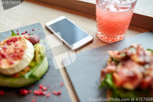 Image of smartphone, glass of drink and food on cafe table