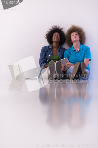 Image of multiethnic couple sitting on the floor with a laptop and tablet