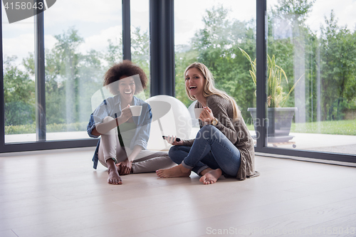 Image of multiethnic women sit on the floor and drinking coffee