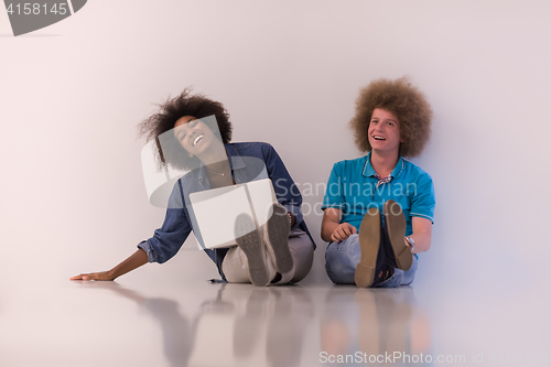 Image of multiethnic couple sitting on the floor with a laptop and tablet