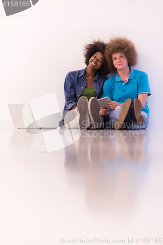 Image of multiethnic couple sitting on the floor with a laptop and tablet