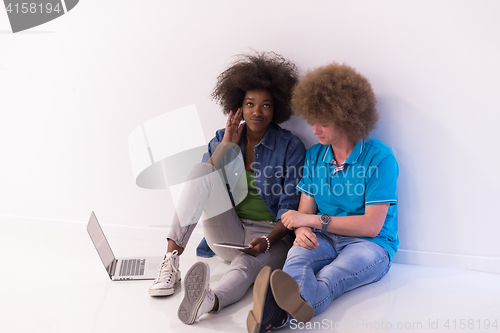 Image of multiethnic couple sitting on the floor with a laptop and tablet