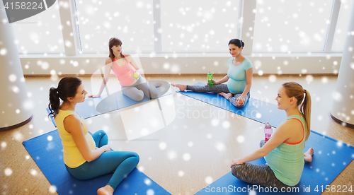 Image of happy pregnant women sitting on mats in gym