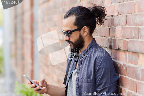 Image of man with backpack texting on smartphone in city