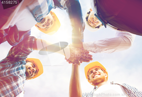 Image of close up of builders in hardhats with hands on top