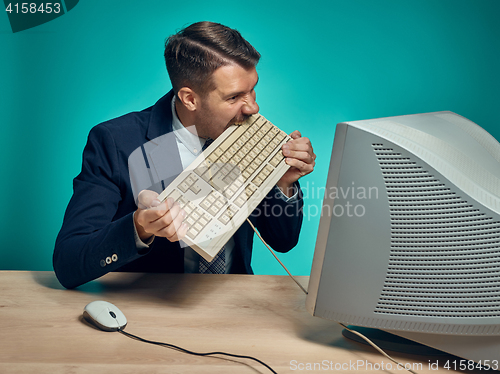 Image of Angry businessman breaking keyboard against blue background