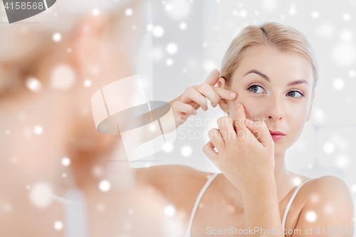 Image of woman squeezing pimple at bathroom mirror