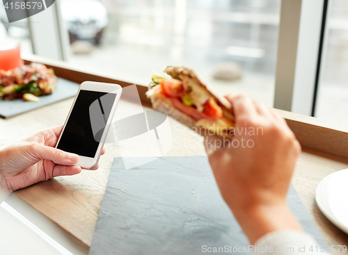 Image of woman with smartphone and sandwich at restaurant