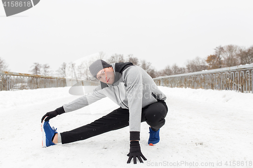 Image of man exercising and stretching leg on winter bridge