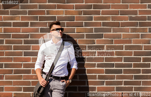 Image of young man in sunglasses with bag over brickwall