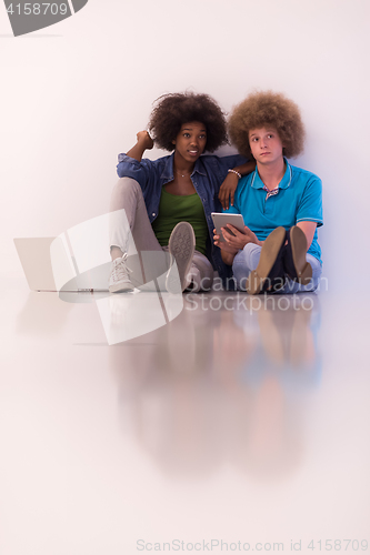 Image of multiethnic couple sitting on the floor with a laptop and tablet