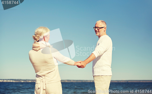 Image of happy senior couple holding hands summer beach