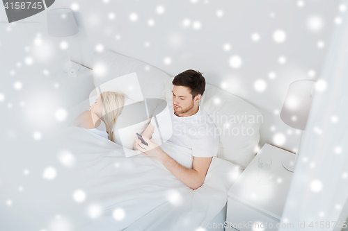 Image of man texting message while woman is sleeping in bed