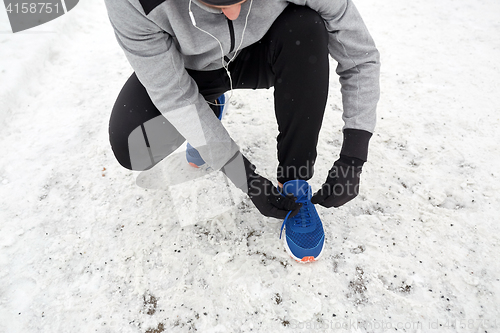 Image of man with earphones tying sports shoes in winter