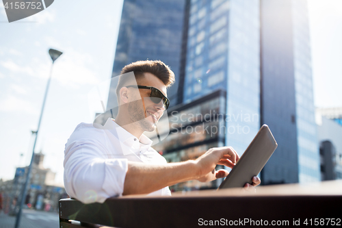 Image of man with tablet pc sitting on city street bench