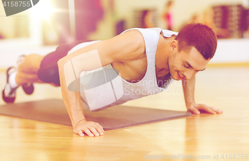 Image of smiling man doing push-ups in the gym