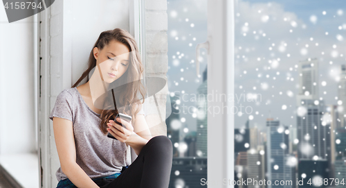 Image of sad pretty teenage girl with smartphone texting