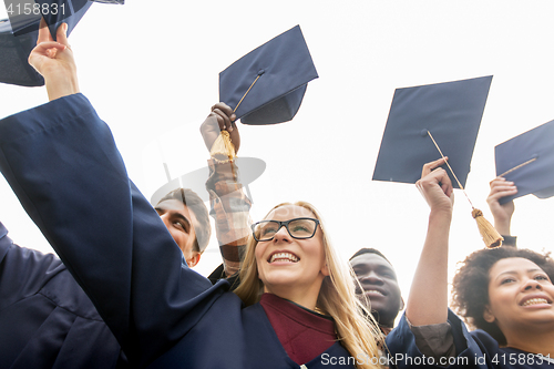 Image of happy students or bachelors waving mortar boards