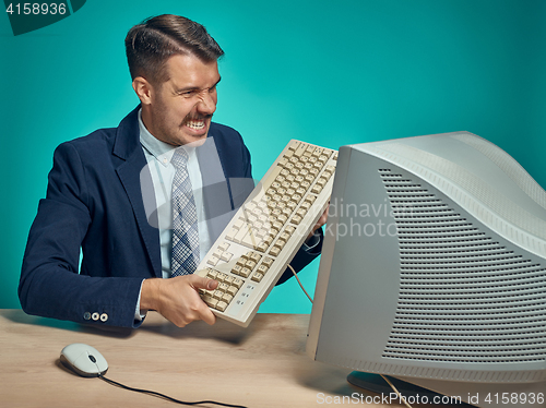 Image of Angry businessman breaking keyboard against blue background