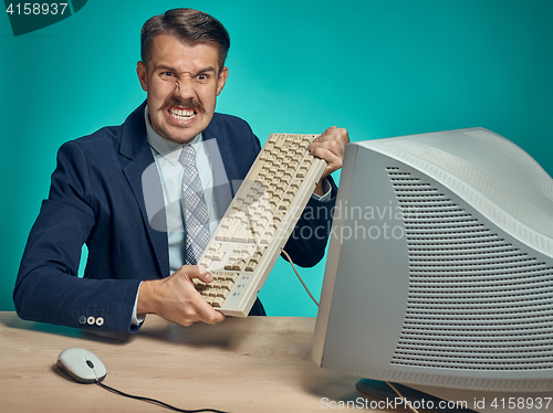 Image of Angry businessman breaking keyboard against blue background