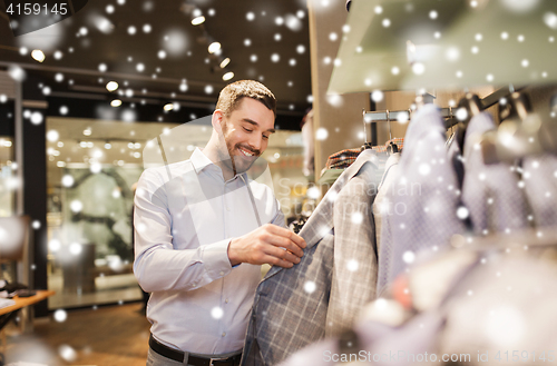 Image of happy young man choosing clothes in clothing store