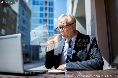 Image of senior businessman with laptop drinking coffee