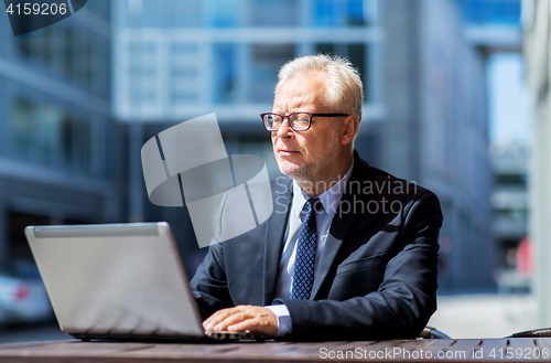 Image of senior businessman with laptop at city street cafe