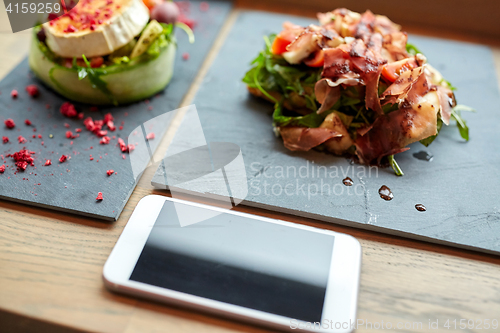 Image of goat cheese and ham salads with smartphone at cafe