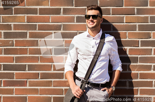 Image of young man in sunglasses with bag over brickwall