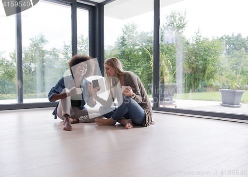 Image of multiethnic women sit on the floor and drinking coffee