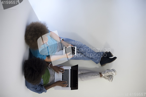 Image of multiethnic couple sitting on the floor with a laptop and tablet