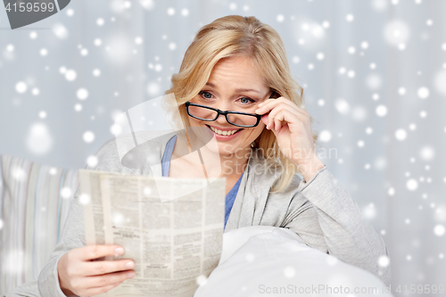 Image of woman in eyeglasses reading newspaper at home