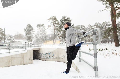 Image of sports man stretching leg at fence in winter